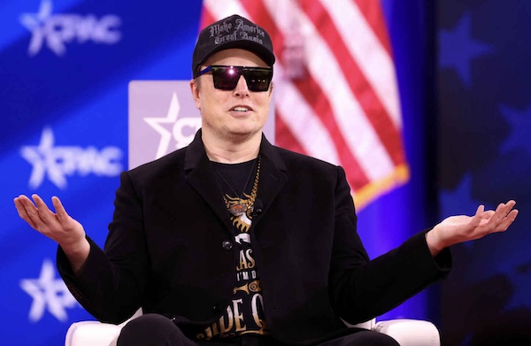 Elon Musk on stage wearing a hat and sunglasses